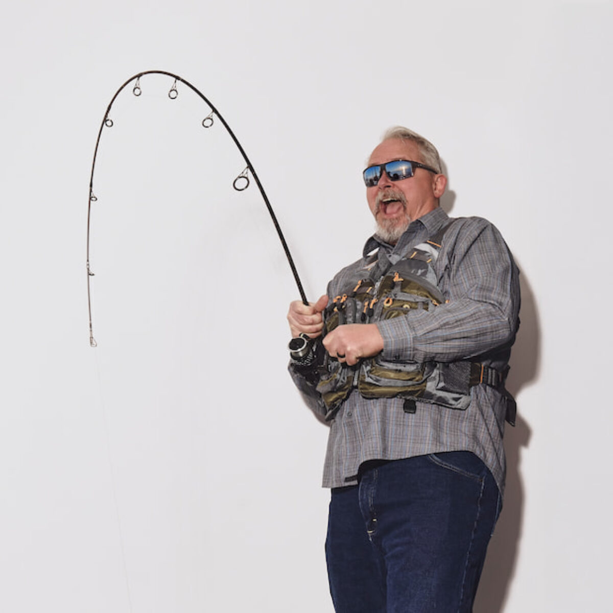 Frank Whanger reeling in a catch with a bent fishing rod, geared up for fly-fishing