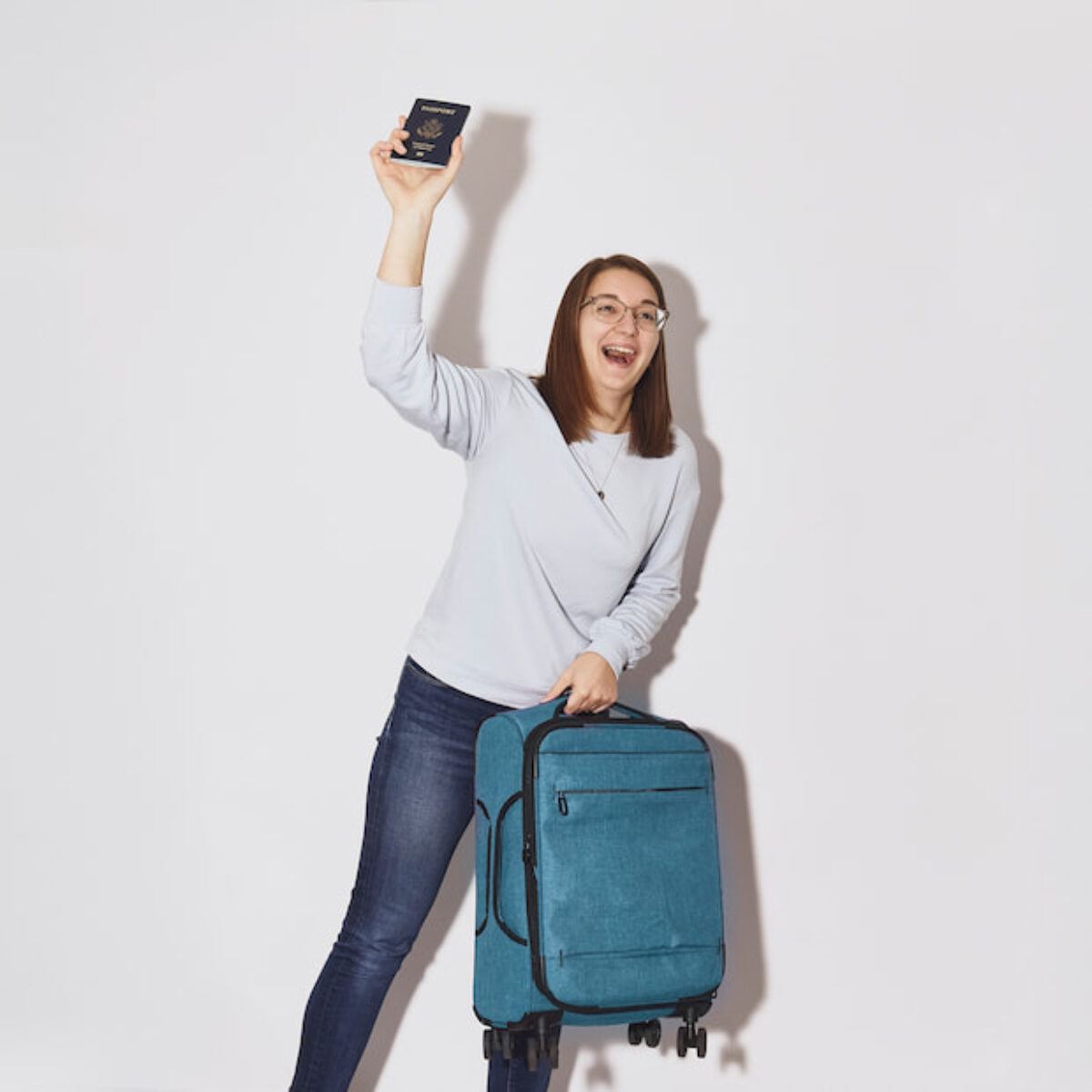 Hannah Miller holding up a passport beside a rolling suitcase, ready to travel
