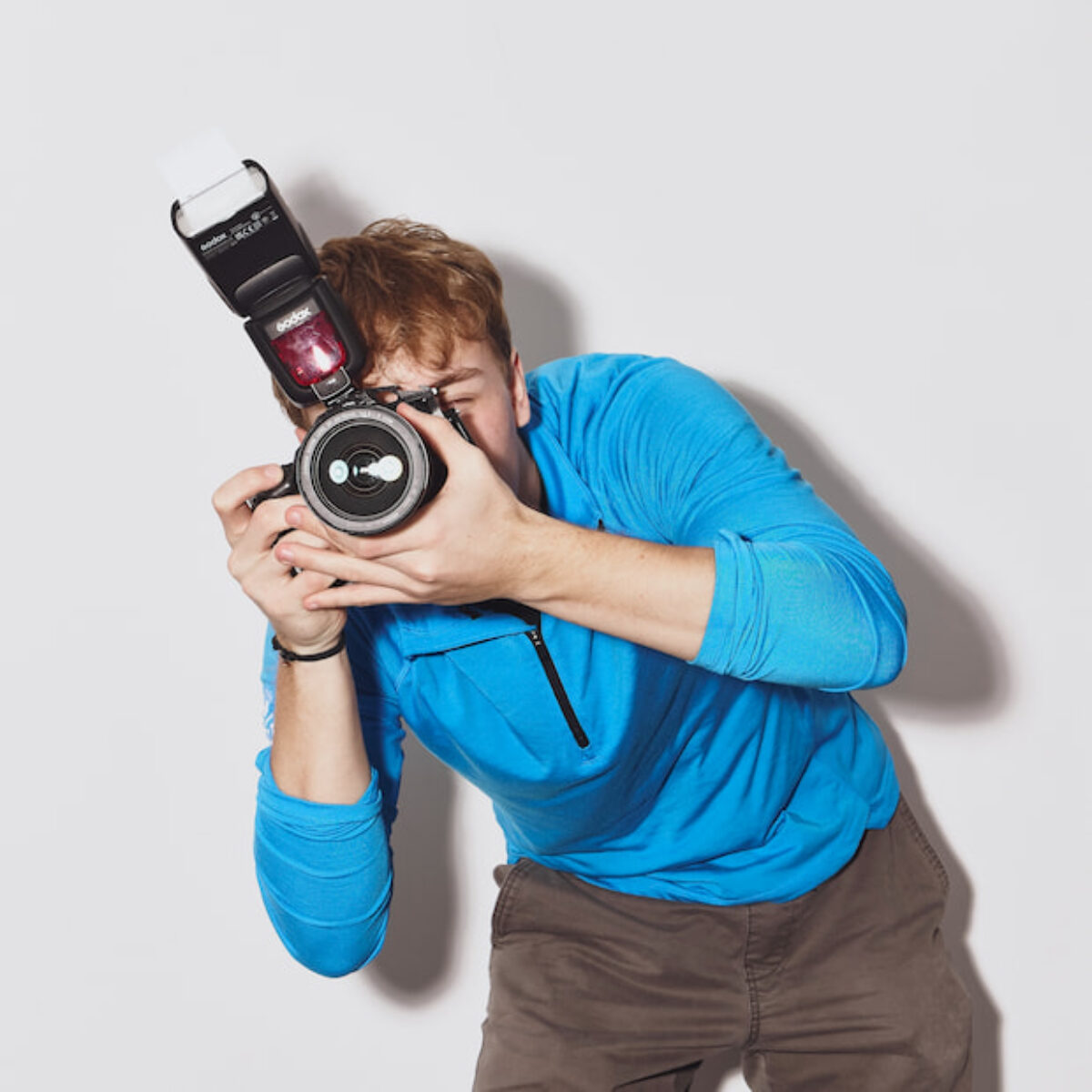 Keegan Bear aiming a camera with an on-camera flash, mid-shot