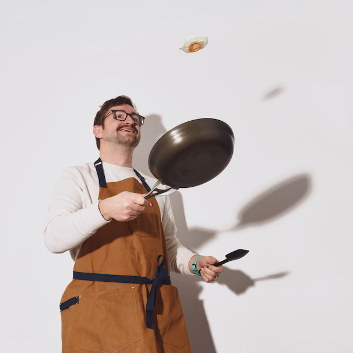 Nathan Van Twisk flipping an egg in a skillet while cooking in an apron